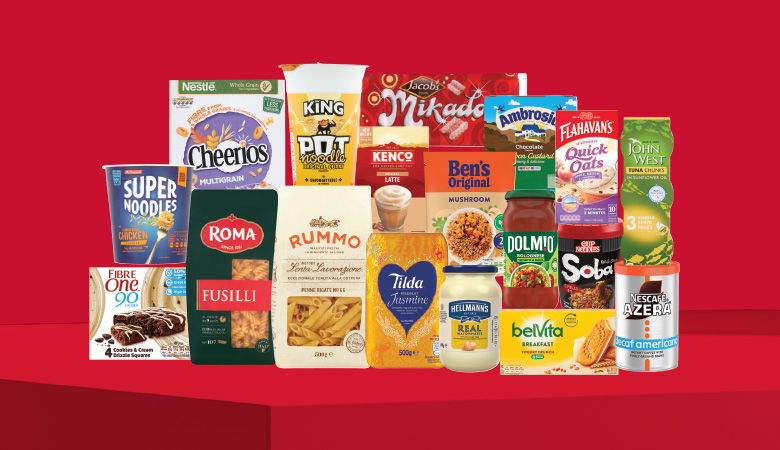 A promotional image displaying various grocery items against a red backdrop. Prominent brands include Cheerios, Jacob's Mikado, Kenco, Ben's Original, Dolmio, Tilda, Hellmann's, and Belvita. The products range from breakfast cereals and biscuits to pasta, sauces, and instant noodles.