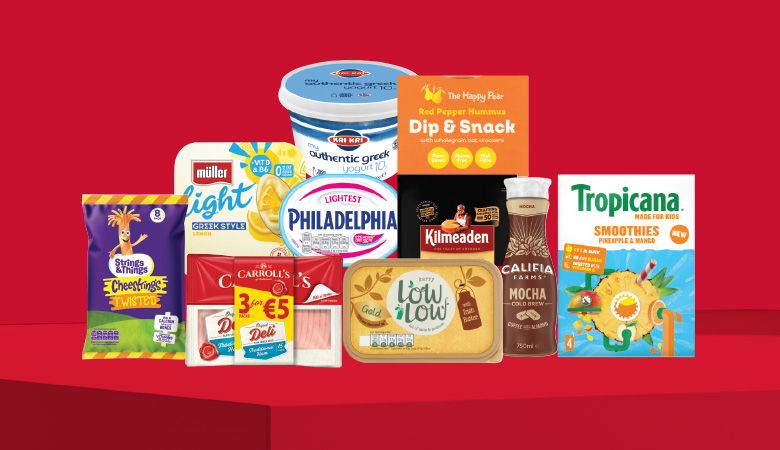 A promotional image showing a variety of food products arranged on a red background. Some of the items include a container of Müller Light yogurt, a pack of Philadelphia Light cream cheese, a jar of Kilmeaden hummus, a bottle of Tropicana smoothies, and various snack packs.