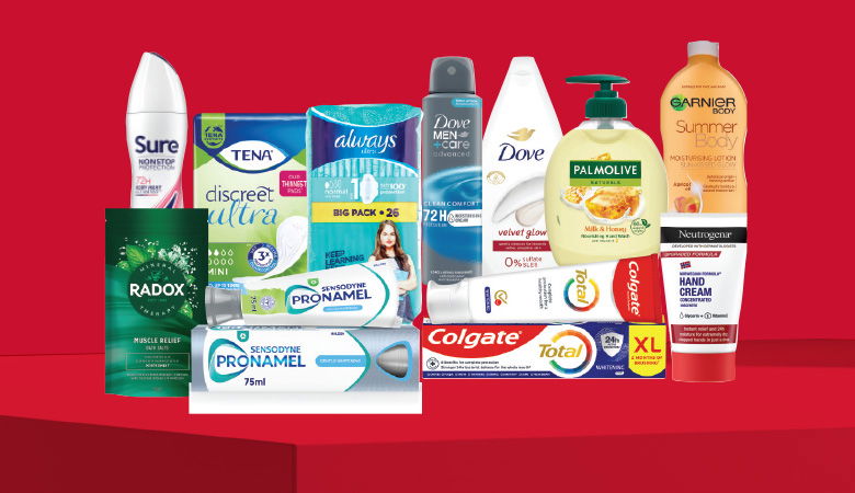 A promotional image showcasing various personal care products against a red backdrop. Featured brands include Sure, Tena, Always, Dove (both men's and women's), Palmolive, Garnier, Neutrogena, Radox, Sensodyne, Pronamel, and Colgate Total.