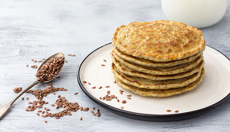 Vegan Pancakes stacked on a white plate, with a spoon of seeds to the side of the plate