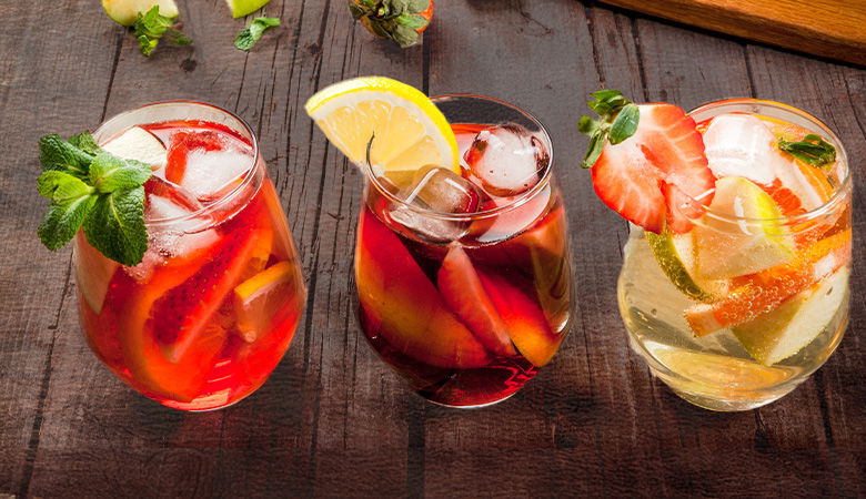 three summer beverages  in a glass with lots of ice and fruit